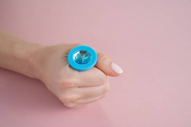 A woman is holding a blue anal plug with a crystal on a pink background. Adult toy for alternative sex - Fotó, kép