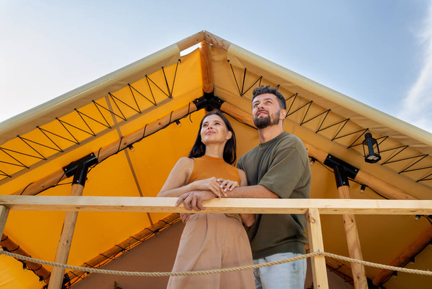 Young serene couple standing by glamping house and looking forwards - Photo, Image