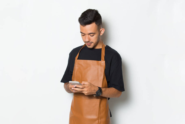Szczęśliwy młody człowiek barista barman lub kelnerka za pomocą telefonu komórkowego smartphone izolowany na białym tle - Zdjęcie, obraz