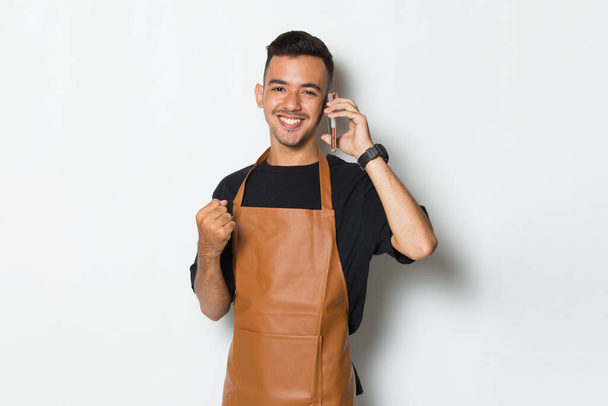 Feliz alegre joven camarero camarero barista o utilizando teléfono inteligente móvil aislado sobre fondo blanco - Foto, Imagen