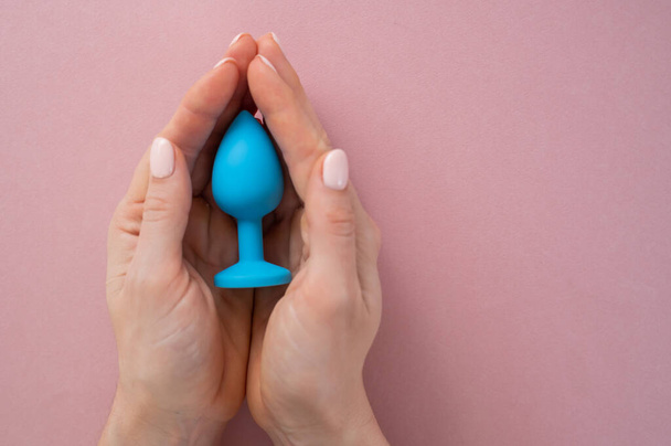 A woman is holding a blue anal plug on a pink background. Adult toy for alternative sex - Фото, зображення