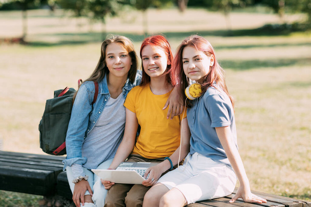 Μια ομάδα έφηβων κοριτσιών κάθεται σε ένα παγκάκι του πάρκου και προετοιμάζεται για τα μαθήματα μαζί, συζητώντας για την εργασία και διασκεδάζοντας. Χρόνος μαζί, φίλοι, φιλία, εκπαίδευση. - Φωτογραφία, εικόνα