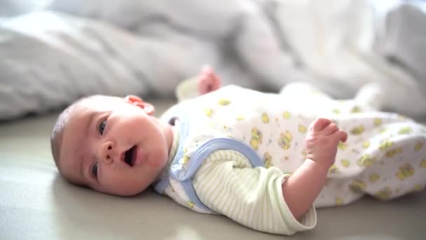 Baby ligt op het bed en heft benen en armen - Video