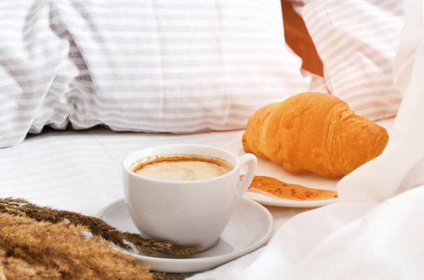 Egy csésze kávé croissant-nal az ágyban. A reggeli kávé fogalma az ágyban. - Fotó, kép