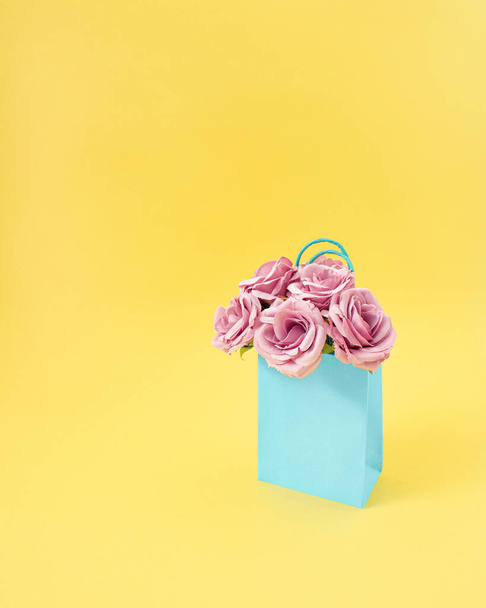 Creative shopping blue bag full of fresh pink roses. A successful shopping day. Flower concept on pastel yellow background. - Foto, Bild