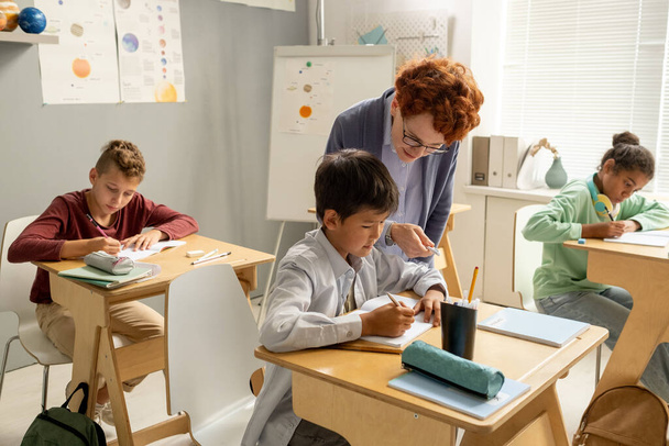 Öğretmen bireysel iş sırasında okul çocuğunun masasına eğiliyor. - Fotoğraf, Görsel