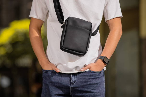 Cropped unrecognizable man holding his new black leather messenger bag in a city - 写真・画像