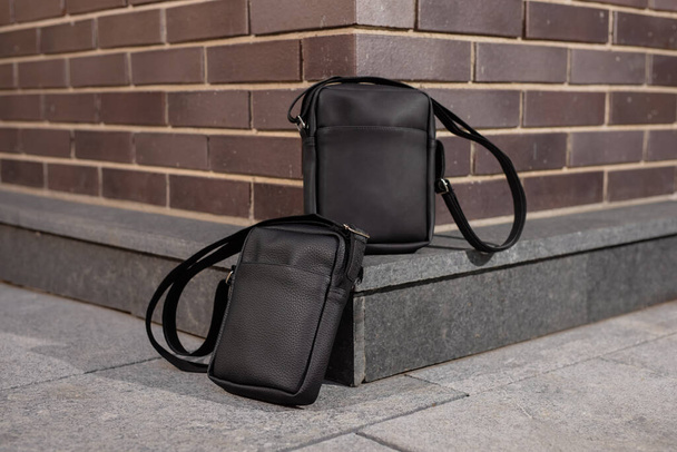 Two black leather messenger bags near brick wall background - Фото, изображение