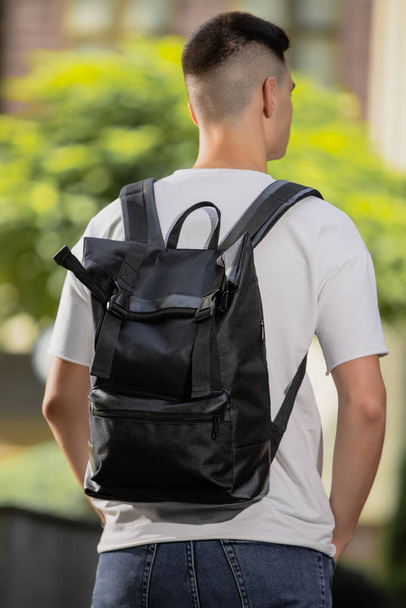 Rear view man walking in city with black leather backpack on his shoulders - 写真・画像