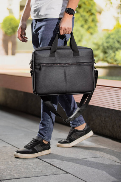 Man walking in city with black leather bag in his hands for laptop computer - 写真・画像