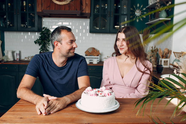 Homme et jeune femme assis dans la cuisine de la maison avec gâteau sur la table - Photo, image