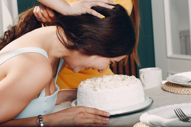 Mladá žena namočí obličej do bílého dortu se smetanou. Happy birthday concept. - Fotografie, Obrázek