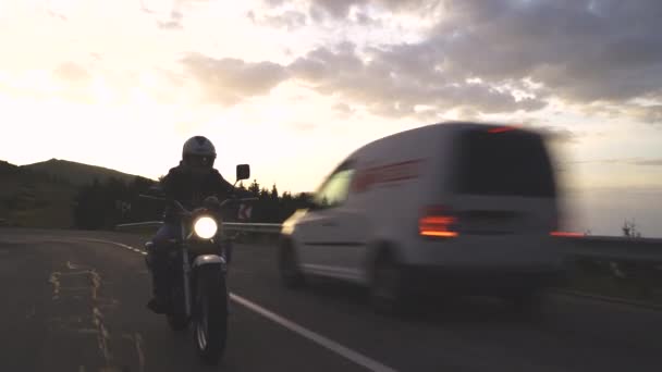 Silhouet van Biker rijden motorfiets op de berg weg passeren auto 's gaan in tegengestelde richting bij zonsondergang - Video