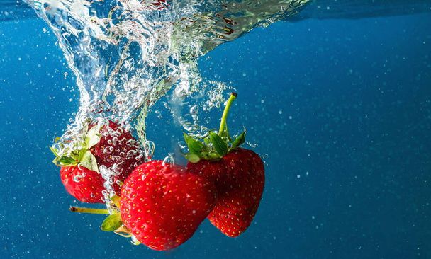 ripe strawberries fall into the water lifting splashes and air bubbles - Zdjęcie, obraz