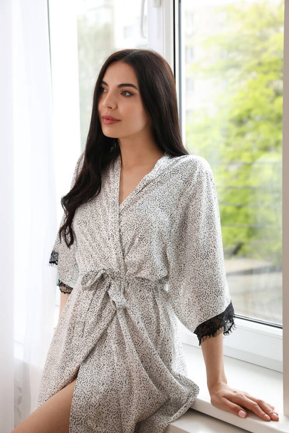 Pretty young woman in beautiful silk robe near window at home - Zdjęcie, obraz