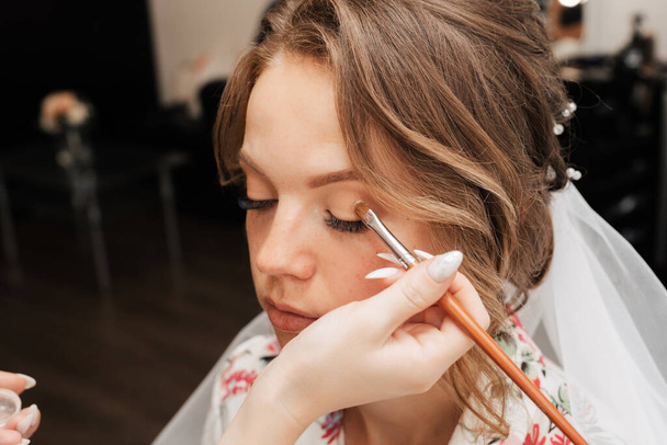 Πυροβολισμοί σε κομμωτήριο. makeup artist εφαρμόζει μακιγιάζ σε ένα νεαρό όμορφο κορίτσι μοντέλο. - Φωτογραφία, εικόνα