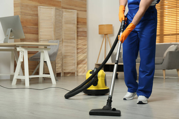 Janitor in uniform vacuuming floor indoors, closeup. Space for text - 写真・画像