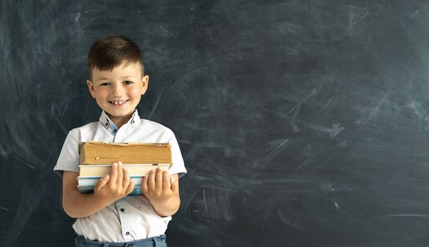 Happy college student standing by the blackboard in the classroom with textbooks or books in hand. Laughing elementary school child. Academic year at the Lyceum. Back to school. Banner. Place for text - Φωτογραφία, εικόνα