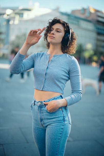 Portrait of a young woman standing in the city square and listening to music. - Foto, afbeelding