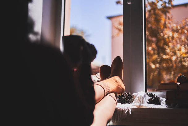 Un acogedor día otoñal. Una mujer colgando sus piernas en el alféizar de la ventana - Foto, imagen
