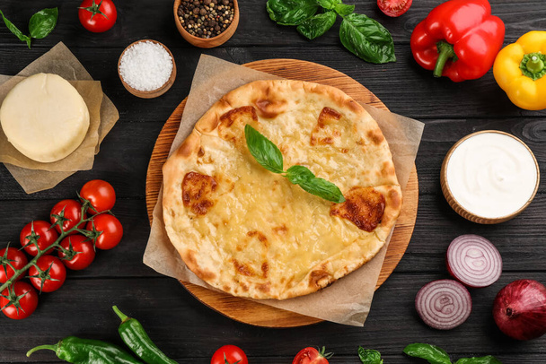 Delicious khachapuri with cheese, sauce, vegetables and spices on dark wooden table, flat lay - Zdjęcie, obraz