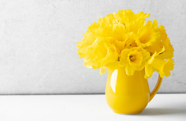 Bouquet of yellow daffodils in a yellow jug on table top, home decor, interior - Foto, Bild
