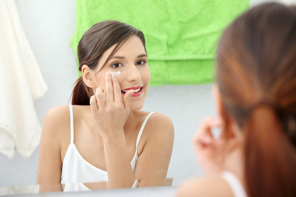 Beautiful woman applying cream on face at bathroom - Foto, Imagem