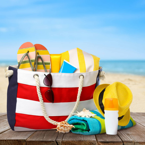 Stylish bag with beach accessories on wooden surface near seashore  - Fotó, kép