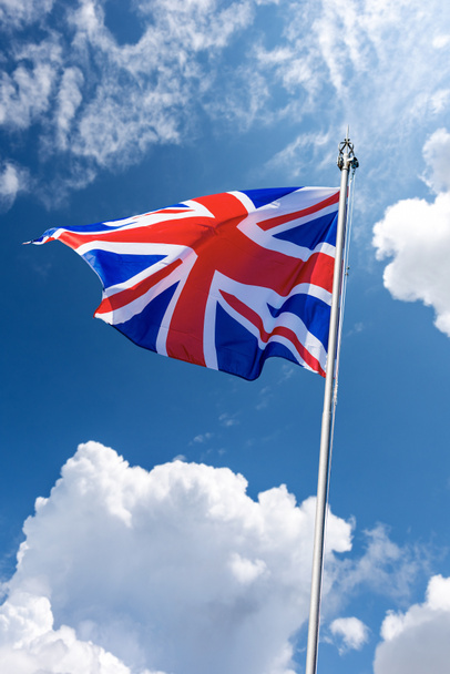 Union Jack Flag. Close-up de uma bandeira nacional do Reino Unido com mastro de bandeira, soprando no vento em um céu azul com nuvens e espaço de cópia. - Foto, Imagem