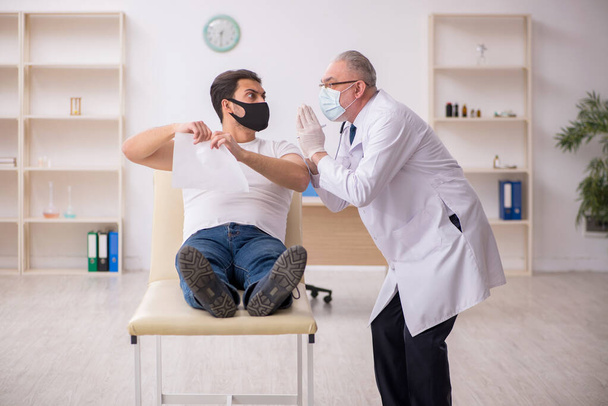 Jovem paciente do sexo masculino visitando o velho médico no conceito de vacinação - Foto, Imagem
