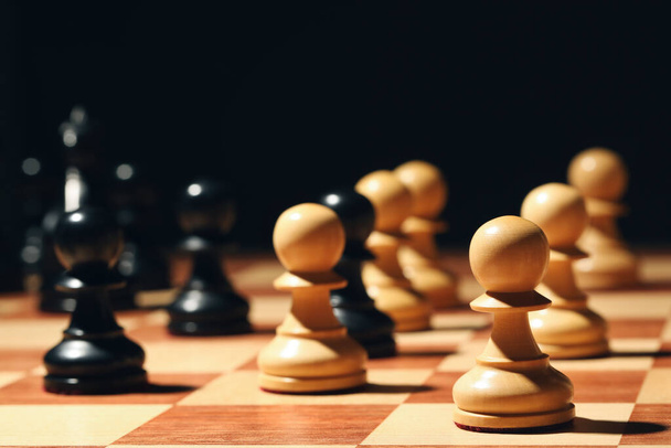 Chessboard with game pieces on black background, closeup - Fotó, kép