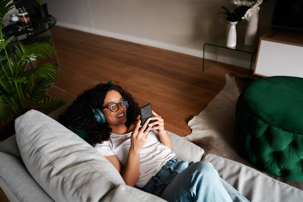 Mixed race female student working from home texting on cellular device listening to music - 写真・画像