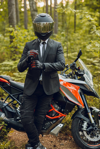 Przystojny rowerzysta z kaskiem i ciemnym motocyklem w lesie - Zdjęcie, obraz