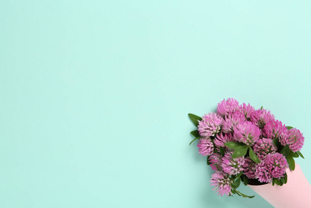 Bouquet of beautiful clover flowers on turquoise background, top view. Space for text - 写真・画像