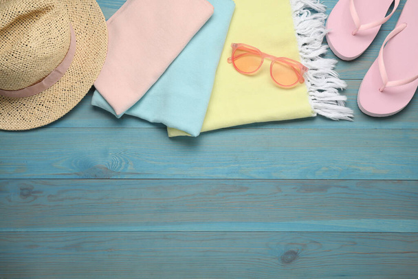Beach towel, flip flops, straw hat and sunglasses on light blue wooden background, flat lay. Space for text - Foto, Imagen