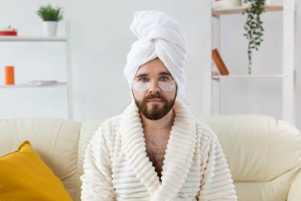 Бородатый мужчина сидит с повязками на лице. Морщины и уход на дому для мужчин. - Фото, изображение