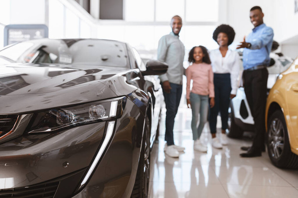 Szczęśliwy młody sprzedawca pomaga afroamerykańskiej rodzinie wybrać luksusowy samochód w salonie samochodowym, selektywne skupienie - Zdjęcie, obraz