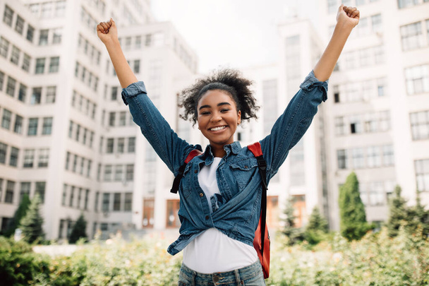 negro estudiante chica sacudiendo puños celebrando éxito en universidad al aire libre - Foto, imagen