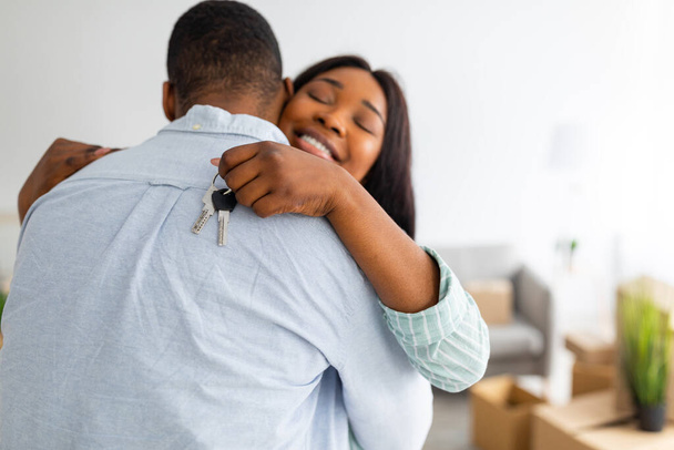 Anahtarlığı olan mutlu siyahi kadın kocasına sarılıyor ve gülümsüyor, evlerine taşınmalarını kutluyor, bedava yer var. - Fotoğraf, Görsel