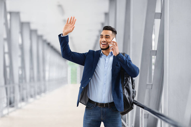 Araber winkt mit der Hand und telefoniert auf Handy, während er im Flughafen geht - Foto, Bild