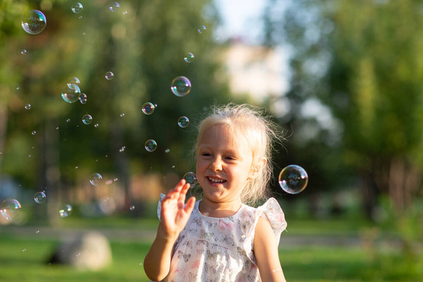 Маленькая милая девочка в летнем парке пускает пузырьки и веселится - Фото, изображение