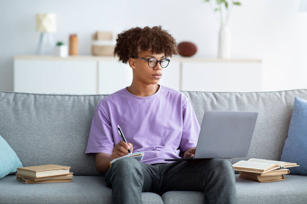 Серйозний афроамериканець, який має онлайн урок на ноутбуці, робить нотатки під час своєї домашньої лекції. - Фото, зображення