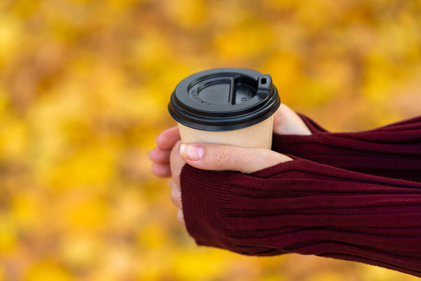 A cozy warm photo of a craft cup of hot coffee in hands against a background of fallen yellow leaves. - Foto, Bild