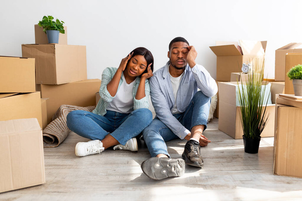 Портрет втомлених афроамериканських подружжів виснажених після переїзду в нову квартиру, які сидять серед коробки з - під картону. - Фото, зображення