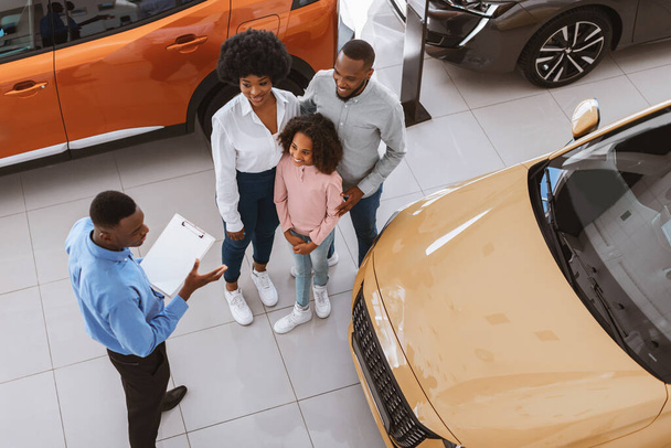 Above view of millennial black family purchasing or renting new car, consulting salesman at auto dealership - Photo, Image