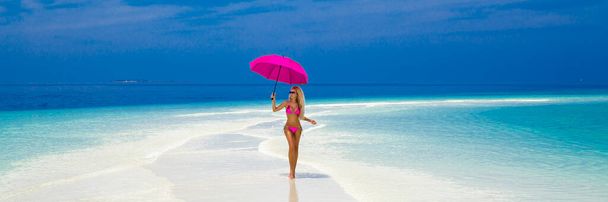 Belle femme sexy bronzée modèle de bikini avec parapluie rose sur l'île des Maldives. Jeune fille glamour en maillot de bain sur le paysage des Maldives. Modèle de bikini corporel parfait. Style de vie de luxe. - Photo, image
