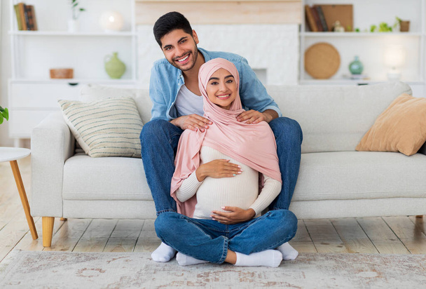 Massage pendant la grossesse concept. Jeune homme arabe massant ses femmes épaules, se reposant ensemble à la maison - Photo, image