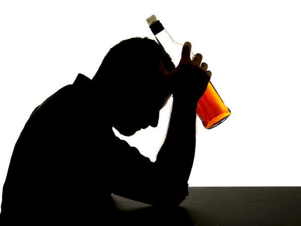 σιλουέτα του αλκοολούχα μεθυσμένος άντρας, κρατώντας το μπουκάλι ουίσκι κατά μέτωπο αίσθημα κατάθλιψη πάσχουν εθισμός στο αλκοόλ και πρόβλημα αλκοολισμού που απομονώνονται σε λευκό φόντο - Φωτογραφία, εικόνα