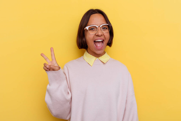 Young student mixed race woman isolated on yellow background joyful and carefree showing a peace symbol with fingers. - Photo, Image