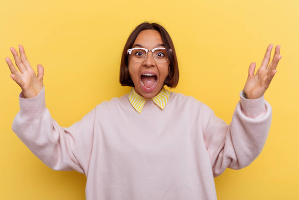 Young student mixed race woman isolated on yellow background receiving a pleasant surprise, excited and raising hands. - Photo, Image